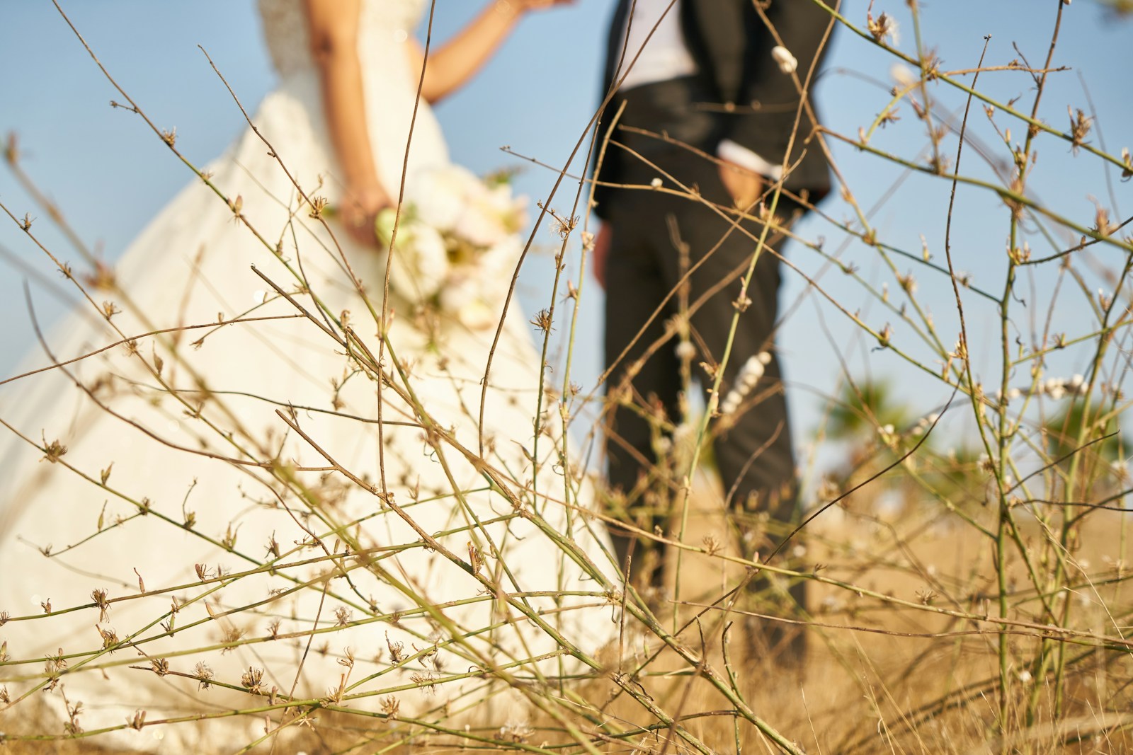 man in black suit jacket and blue denim jeans standing beside woman in white wedding gown